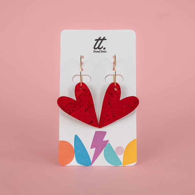 Red heart-shaped earrings on a branded card with colorful designs against a pink background