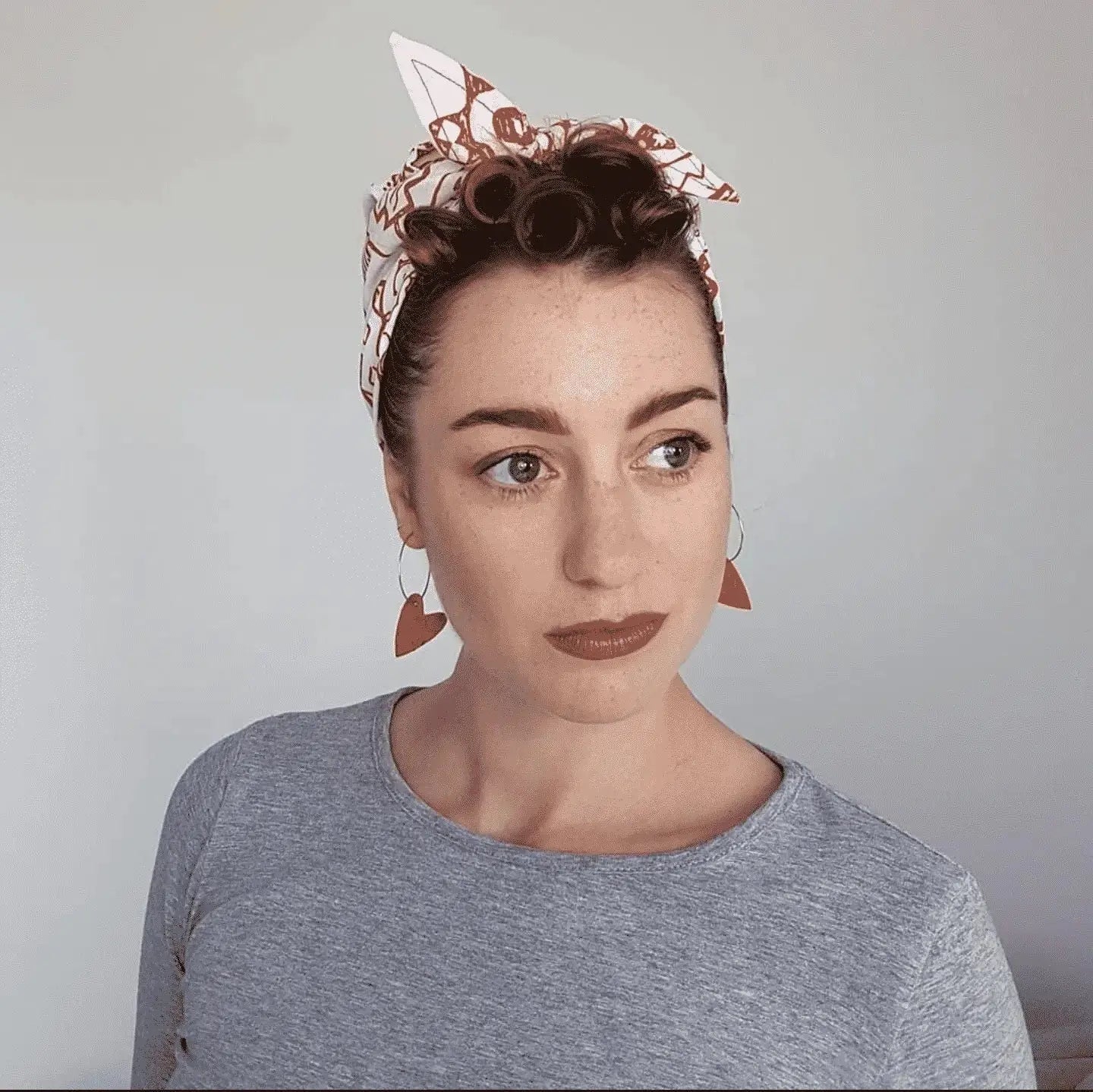 Woman with hair rollers and a headband against a plain background