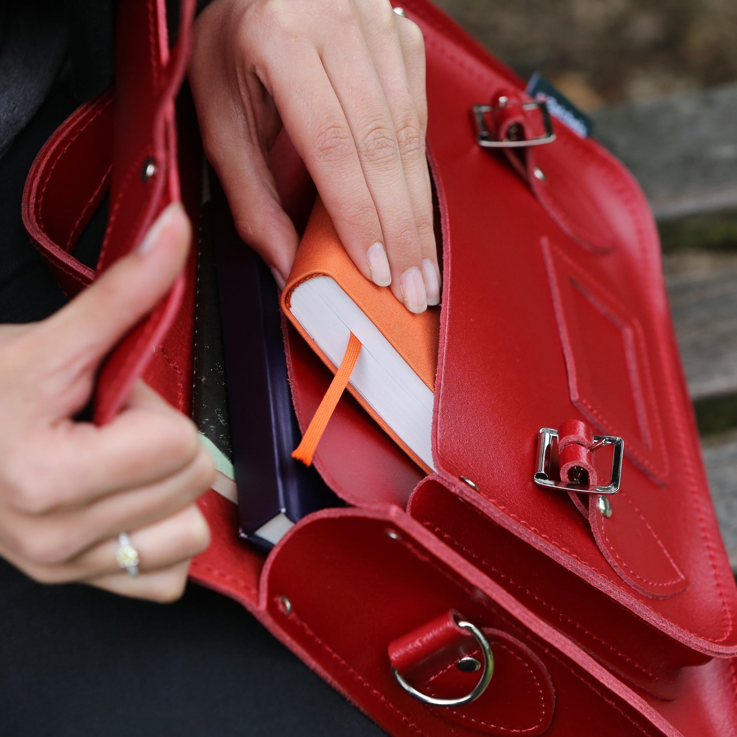 Red handbag with books and a phone inside, held by a person.