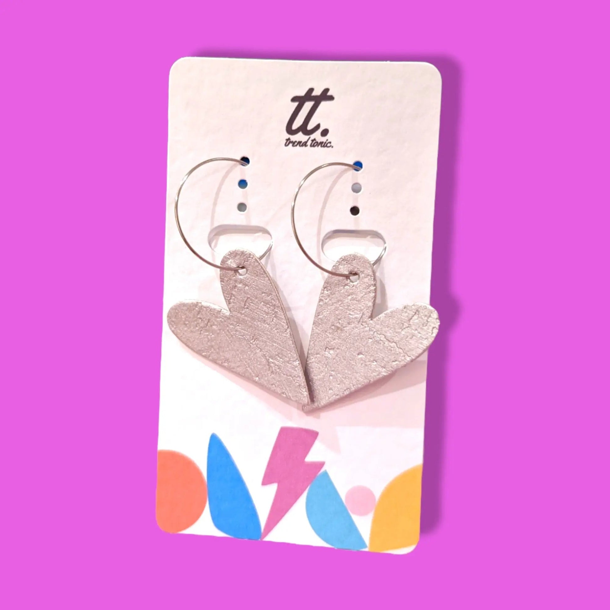 Heart-shaped earrings on a Trendy Tonic card against a pink background