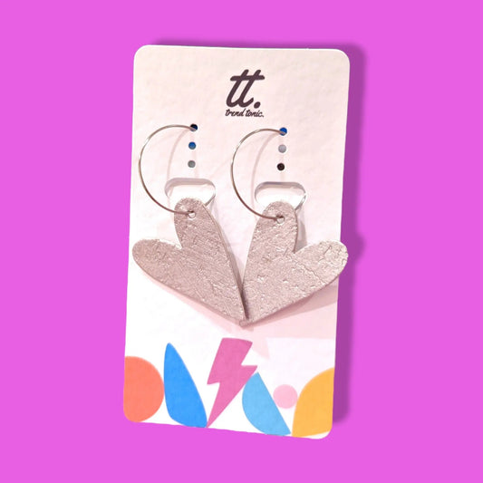 Heart-shaped earrings on a Trendy Tonic card against a pink background