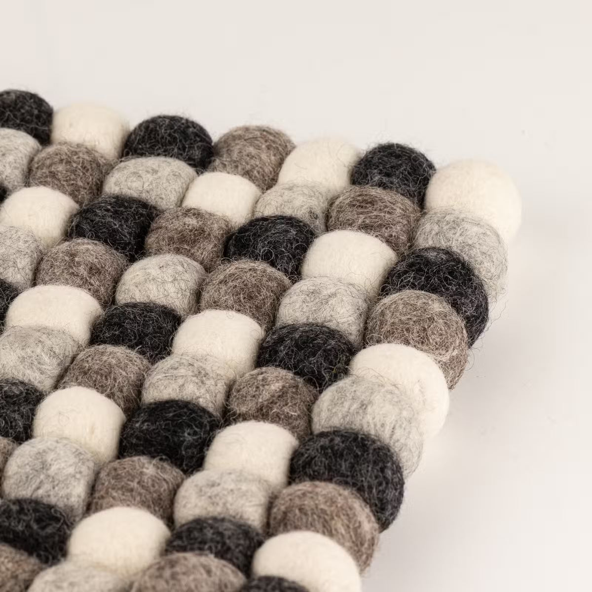 Close-up of one corner of the grey felt ball square placemat, showing charcoal, grey, taupe and cream wool balls