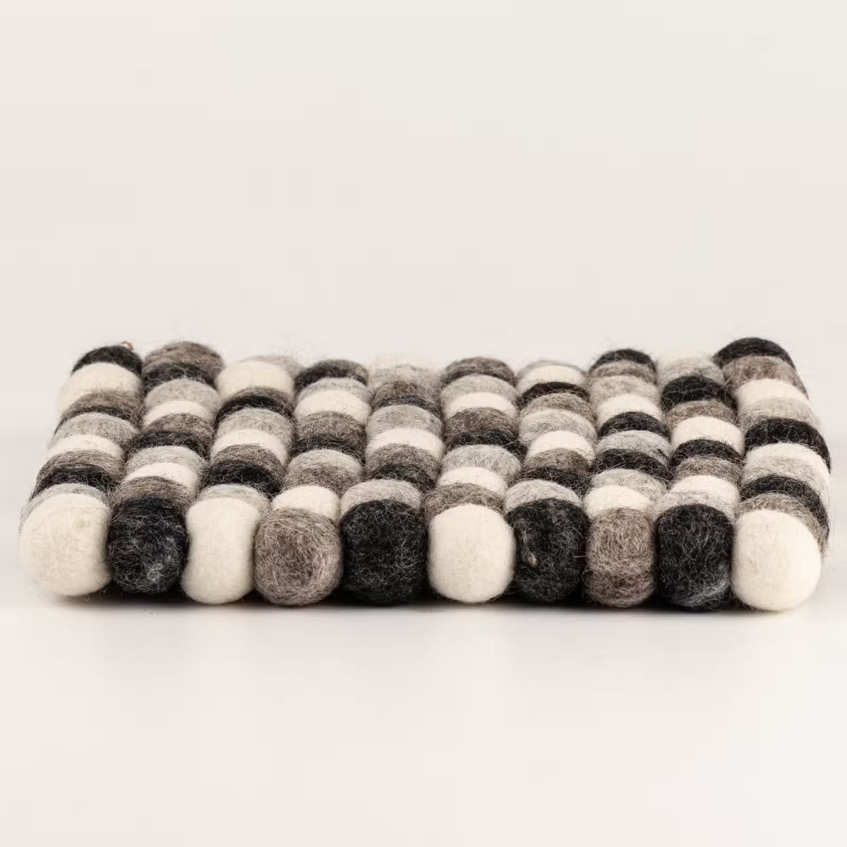Side view of the grey felt ball square placemat showing its 2cm thickness