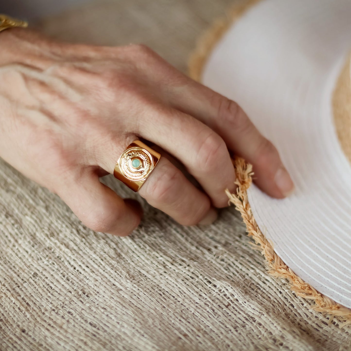 Hand wearing a gold ring with a green stone on a textured surface