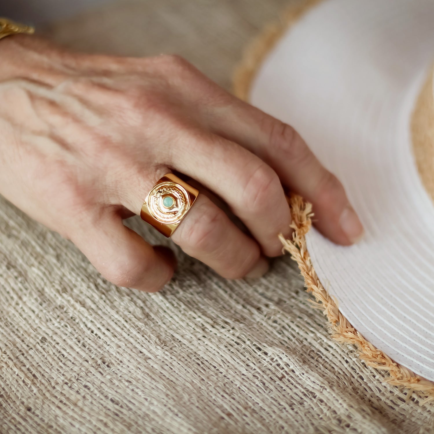 Hand wearing a gold ring with a green stone on a textured surface